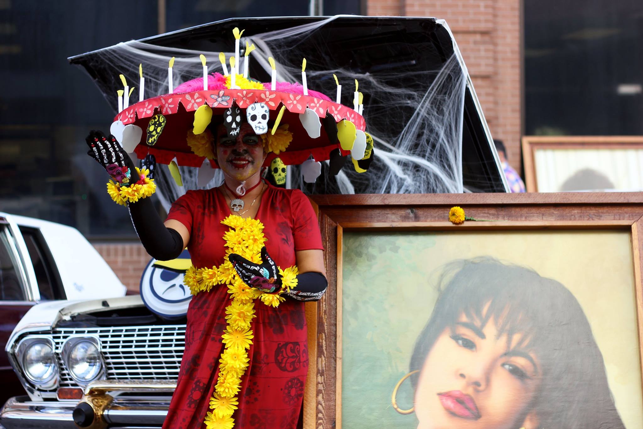   A woman dressed as La Calavera Catrina poses next to a painting of Selena Quintanilla.  