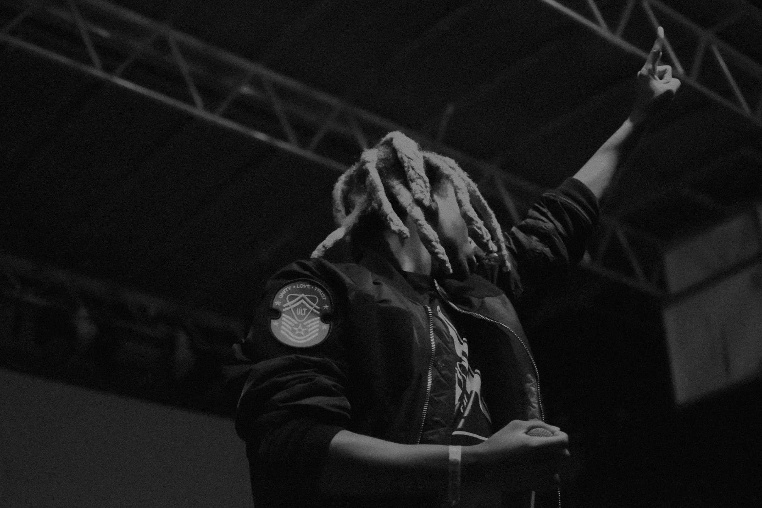   Denzel Curry wears a bomber jacket while performing on stage.  