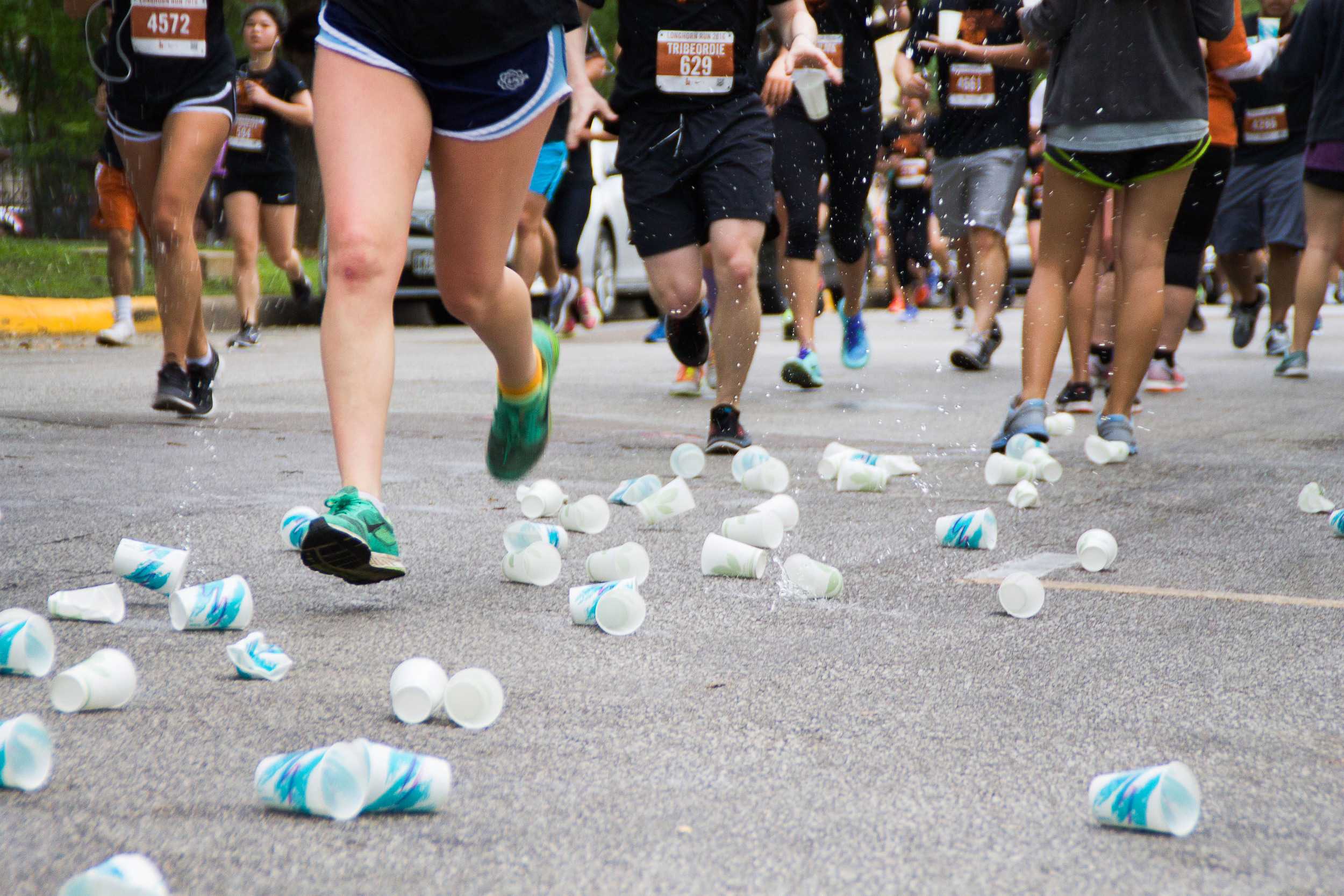  Splashing around runners’ ankles, used water cups crash to the ground at a water station on Whitis Avenue.&nbsp;    