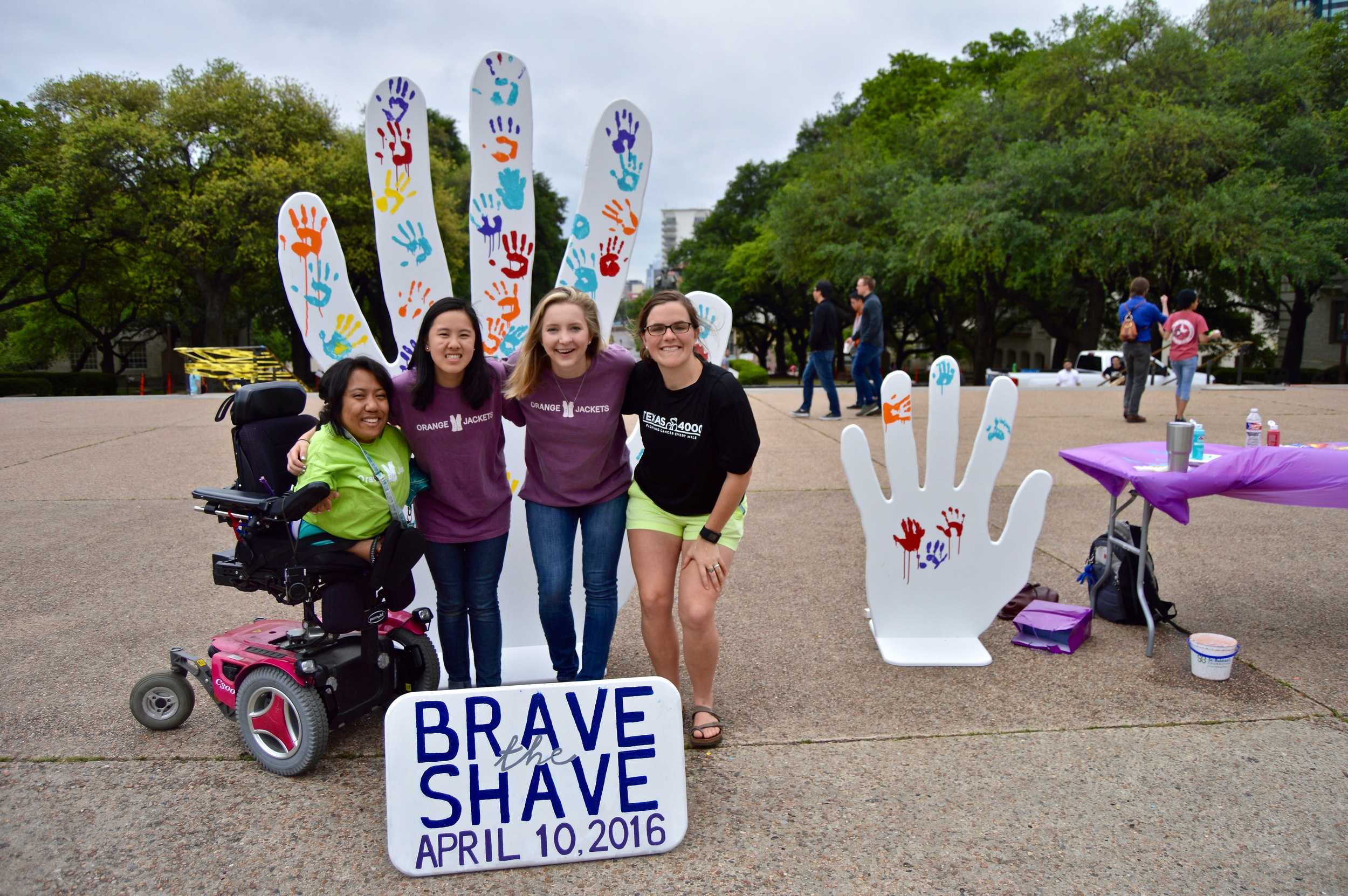   Four volunteers in front of the hand symbol for Brave the Shave.   