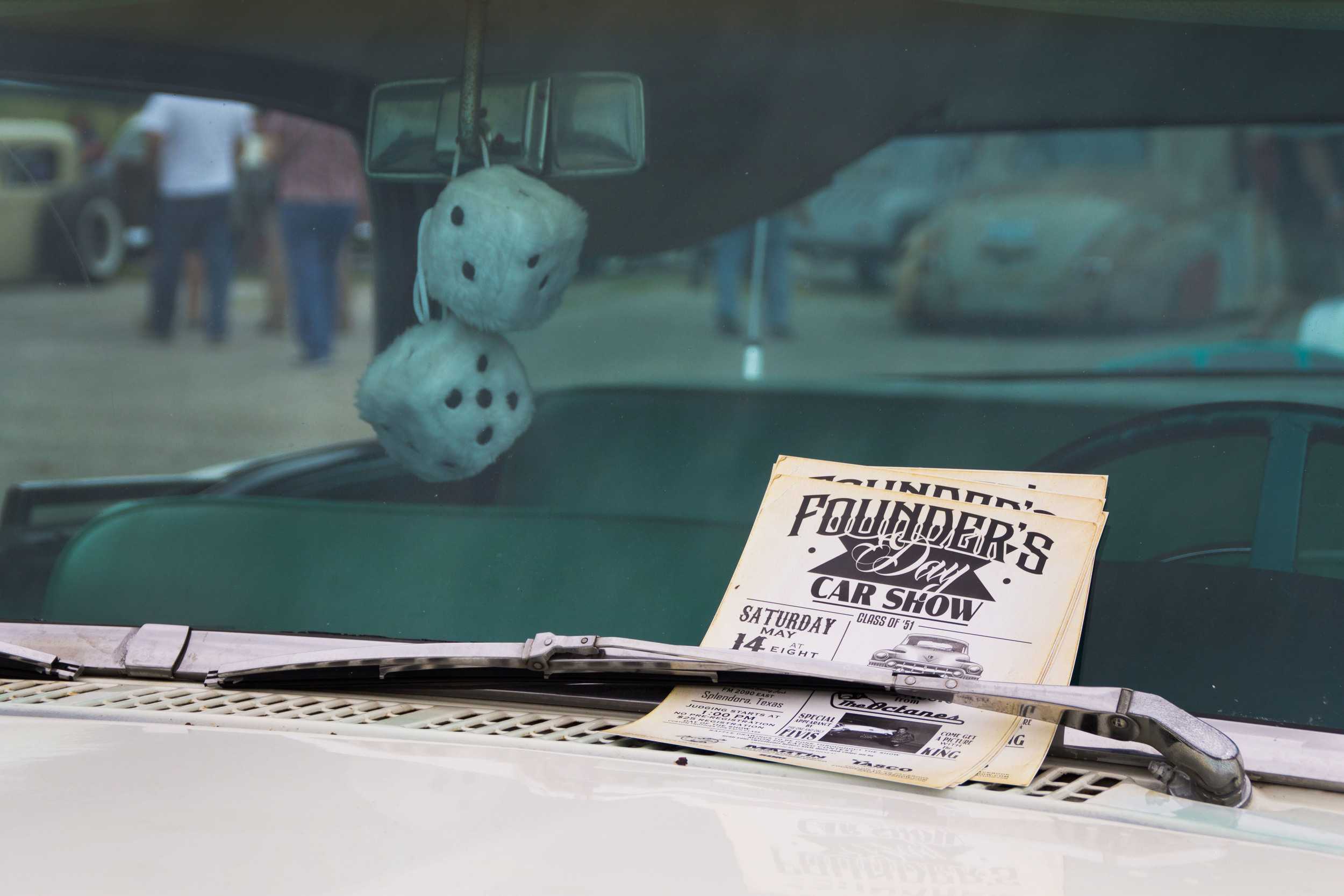  Advertisements for another upcoming car show are fastened under the windshield wipers of a display car, trademark fluffy dice dangling from the rearview mirror. 