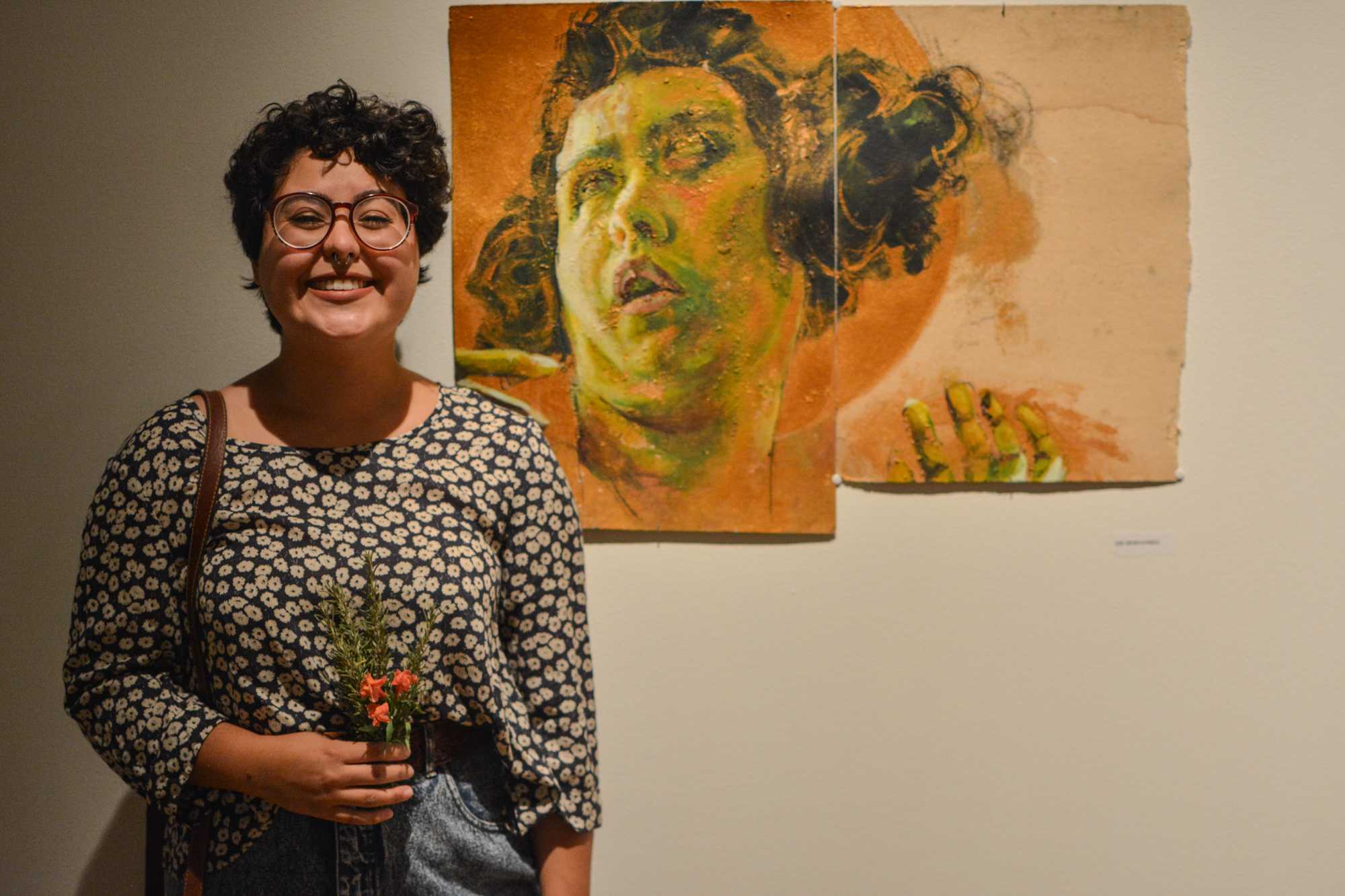   Abi Hernandez smiles widely near her piece at the Study Abroad Art Show in the Visual Art Center. Her art piece is made on cardboard she found lying around in Italy.  