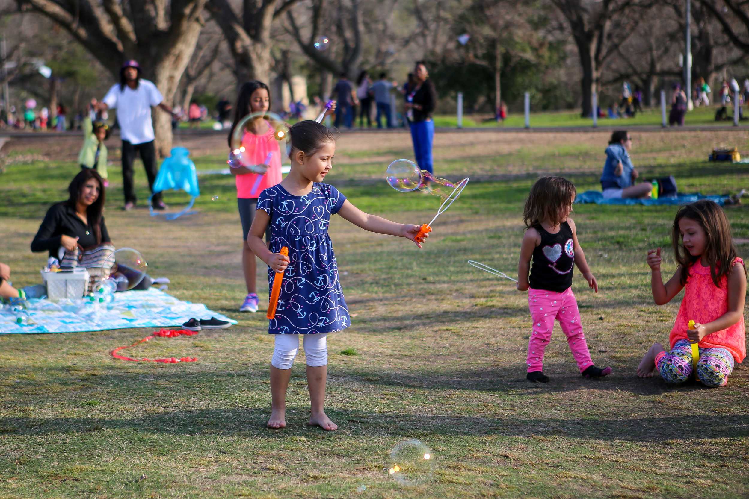  Families and children enjoy the excellent weather at Zilker Park. A girl takes a break from flying a kite to blow some bubbles.&nbsp; 