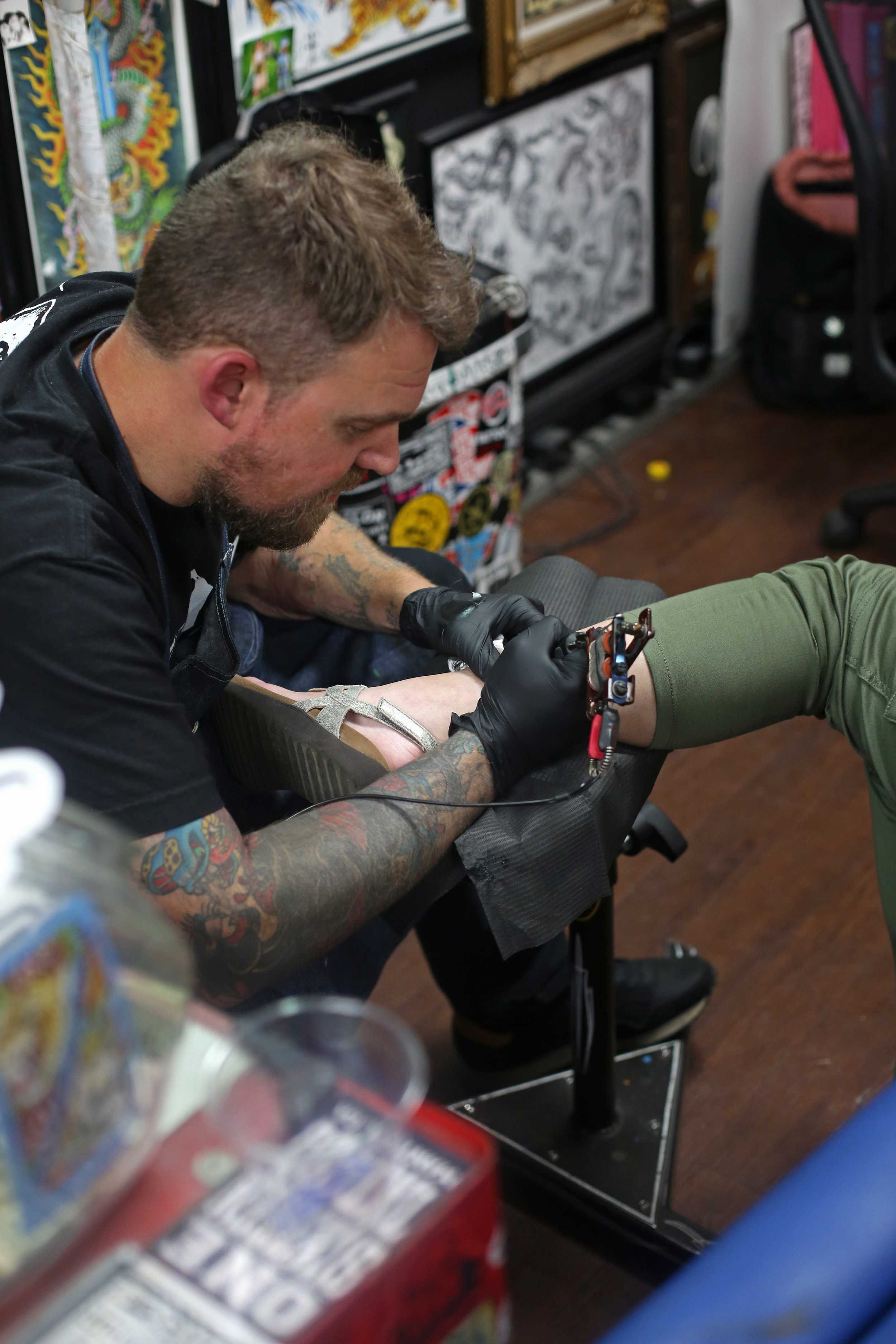   Chris Cotner tattooes a traditional design on a customer’s ankle.  