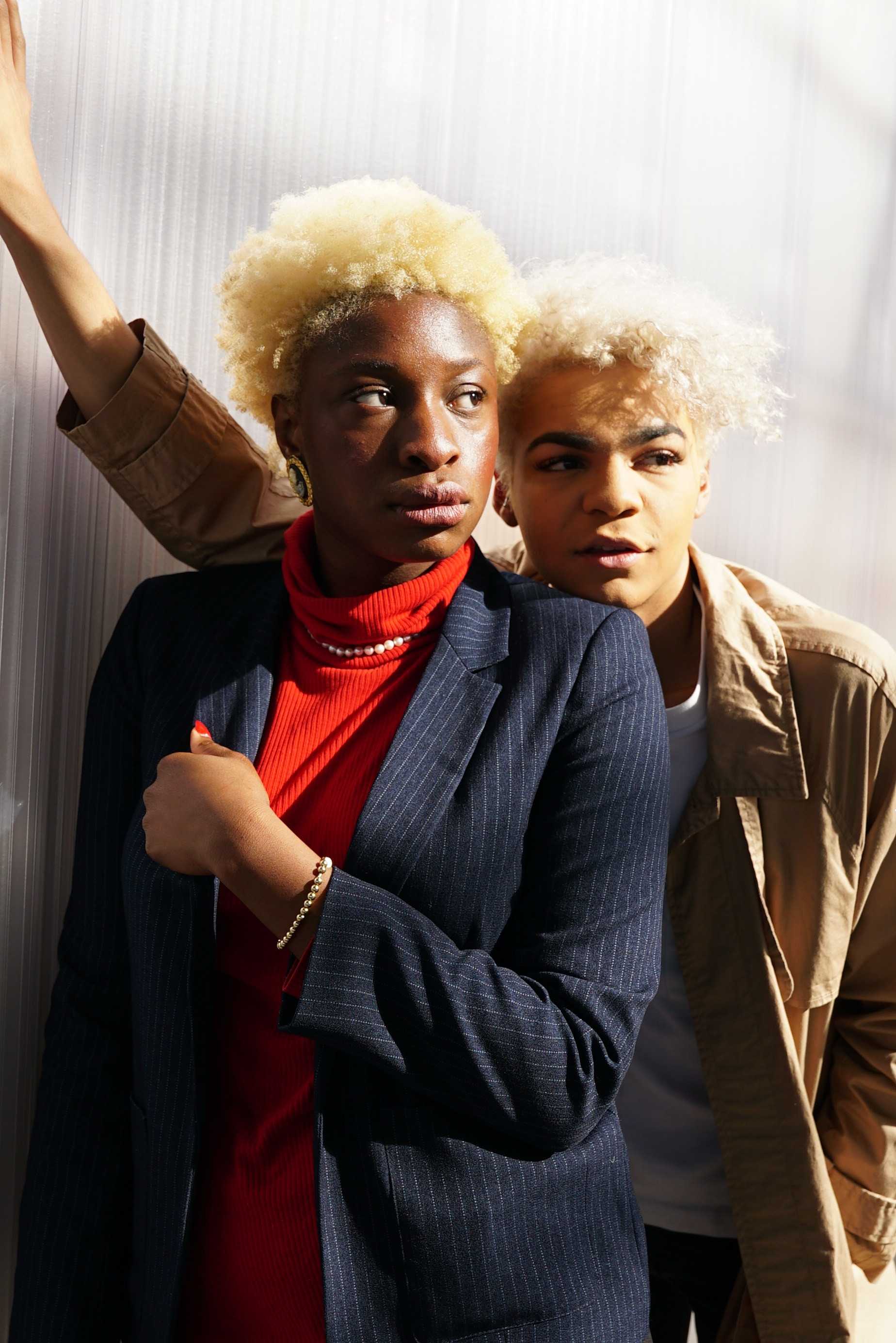   Junior Onome Amudo wears a bright red turtleneck with a complementary pin-striped blue blazer as sophomore Dev Lewis stands behind her in a casual white tee and trench coat combo.  