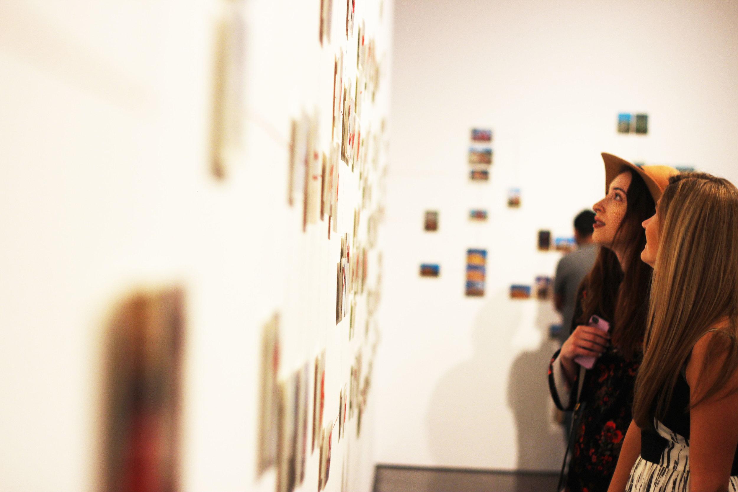   People walk through walls of “Paranormal Postcards”, a series a part of of the newly installed &nbsp;“Curiouser” that interconnects a world view through postcards and red thread.  