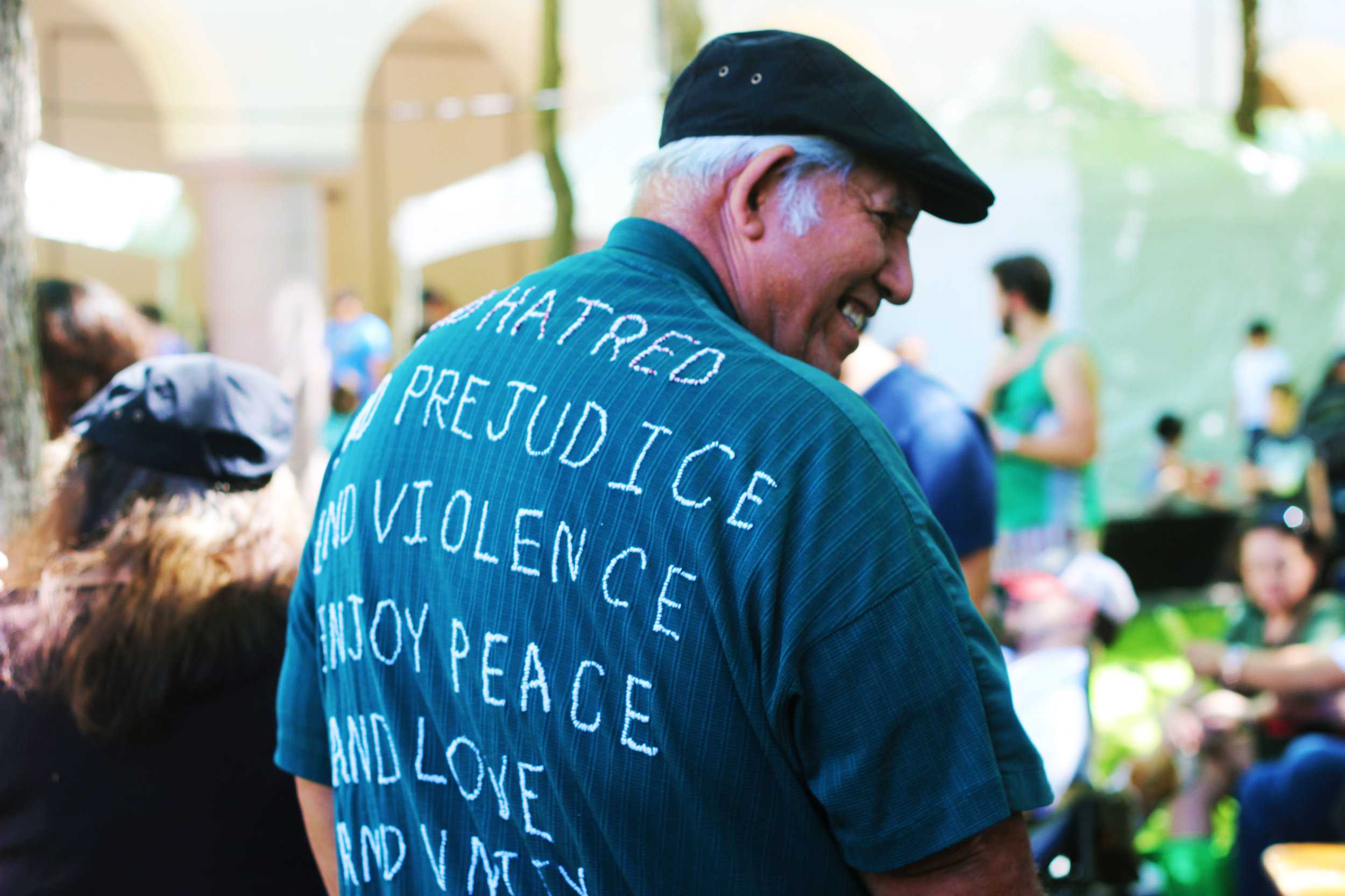   After clapping along to a performance by the UT Austin Mariachi Ensemble, Enrique Cantu shows off the back of his shirt. Embroidered by his wife, the message reads, "End Hatred and End Prejudice and End Violence. Enjoy Peace And Love and Unity."  