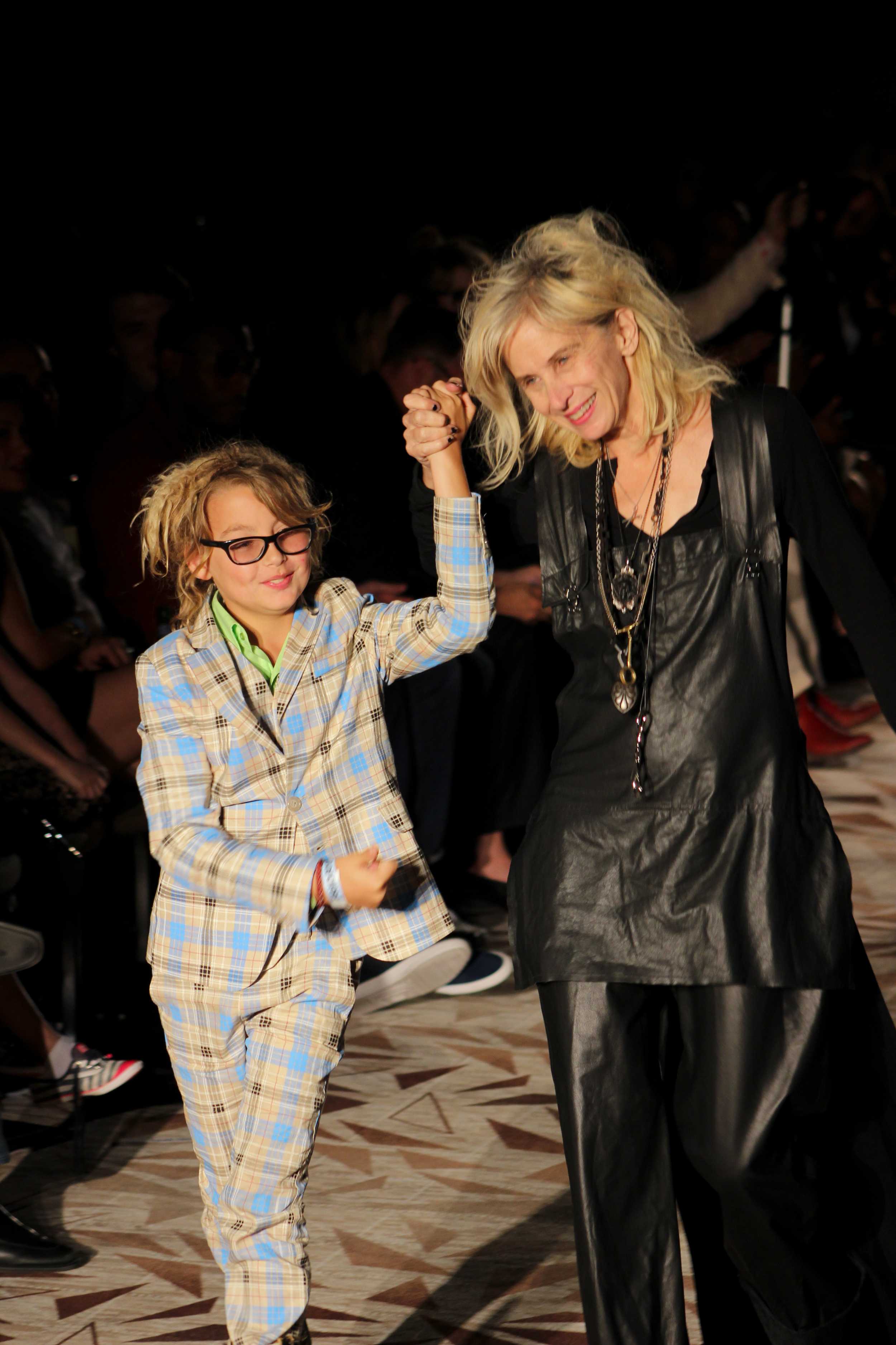   Gail Chovan smiles with her son as she walks down the runway after showing her collection. Photo by Miranda Chiechi.  