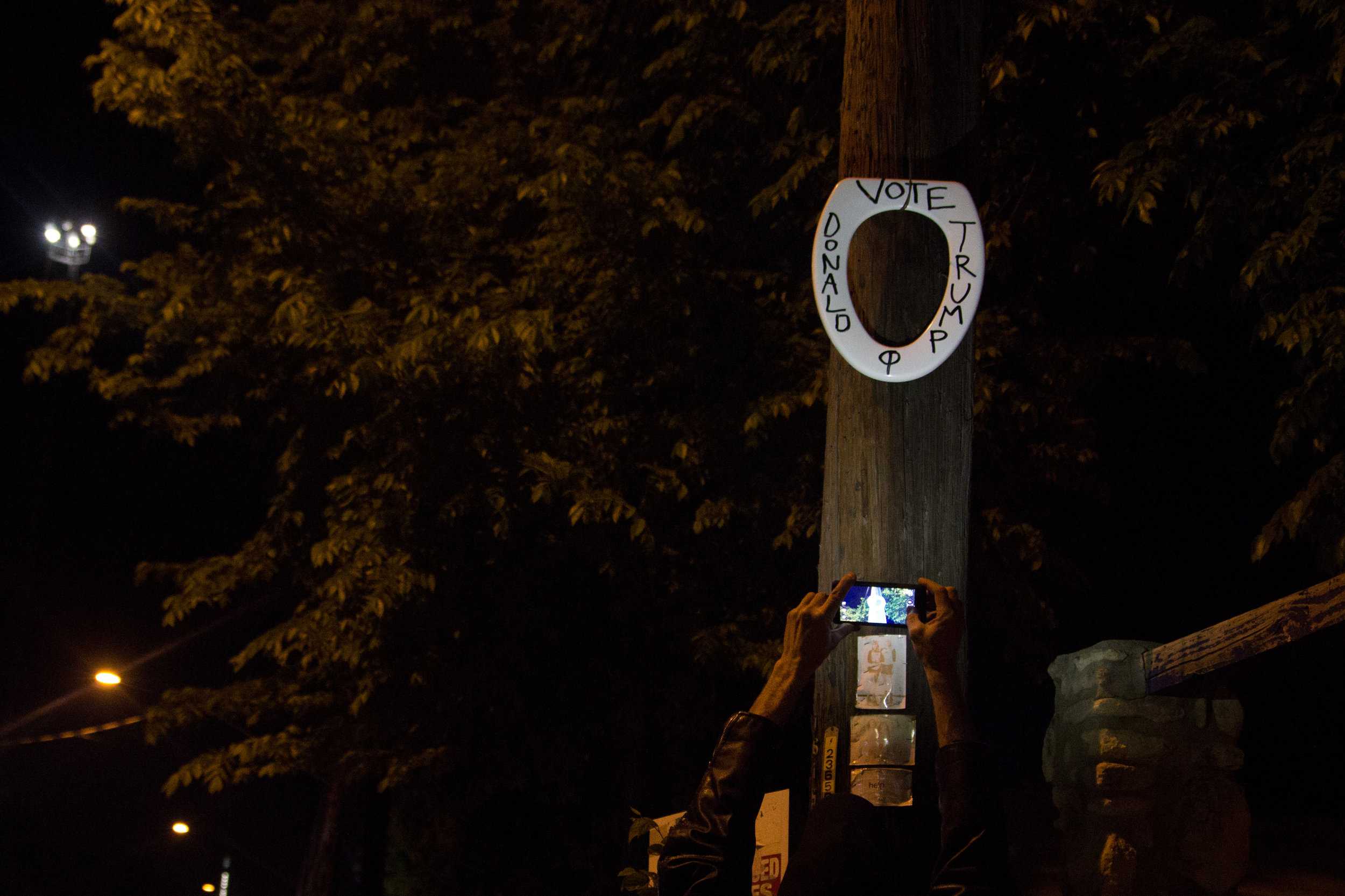   RabbitSnake photographs a “Vote Donald Trump” toilet seat he’d just placed outside of Jovita’s, a restaurant that was shut down following a drug raid.  