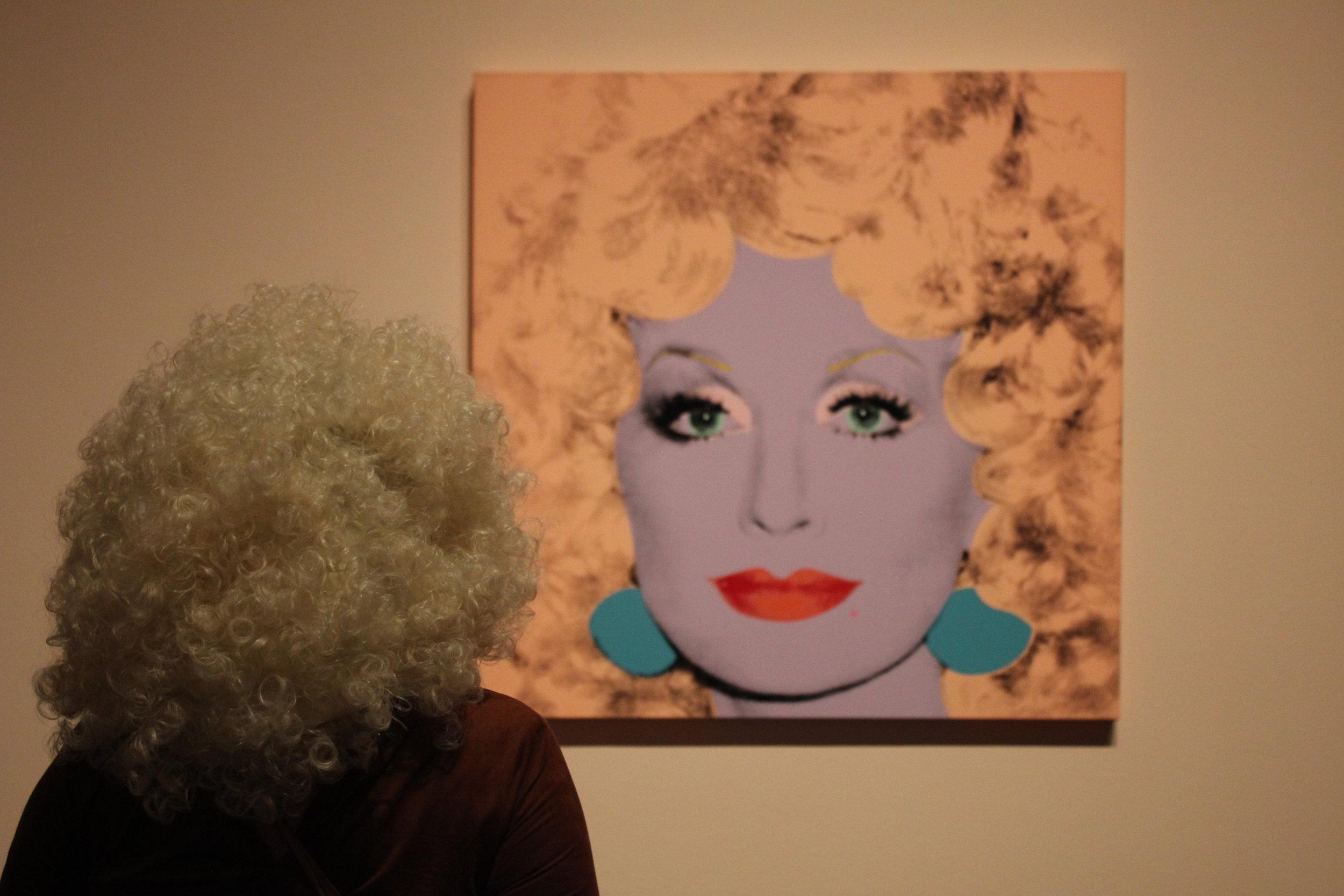   An attendee dressed as Dolly Parton admires the pop-country icon’s portrait.  