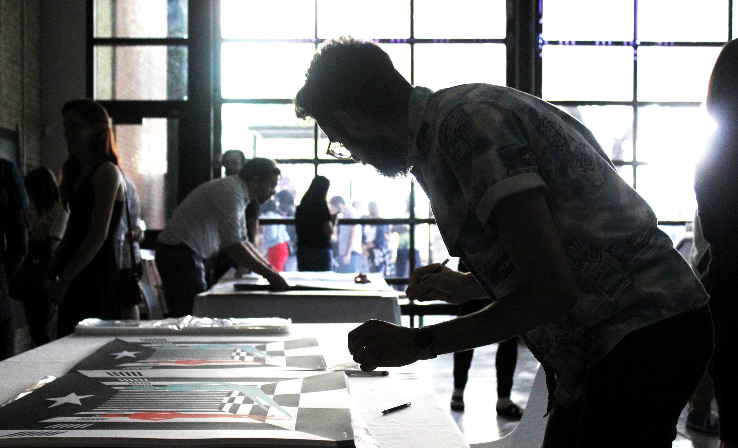   An artist signs copies of his artwork.  