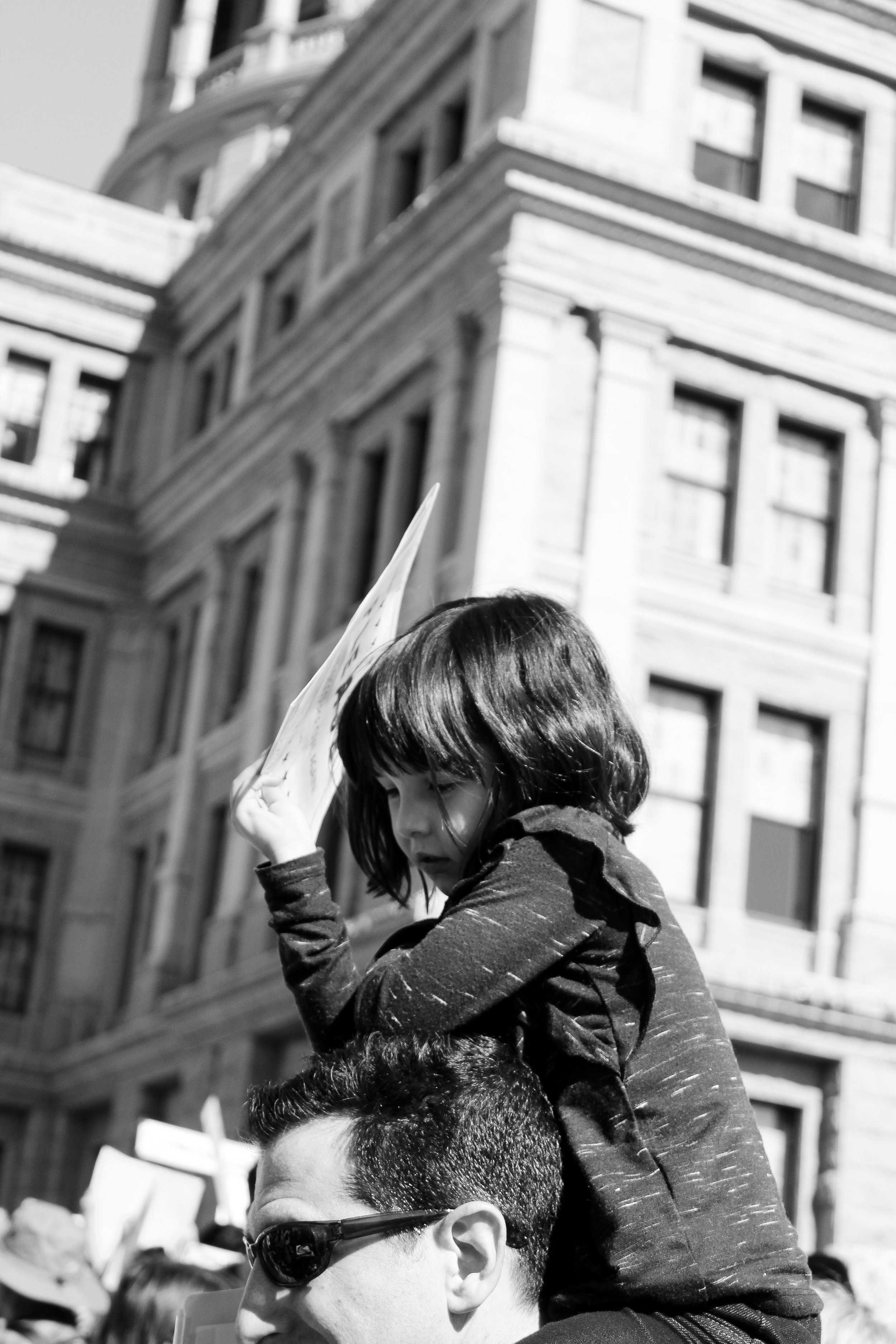   A little girl sits atop her dad’s shoulders, joining the other marchers.     