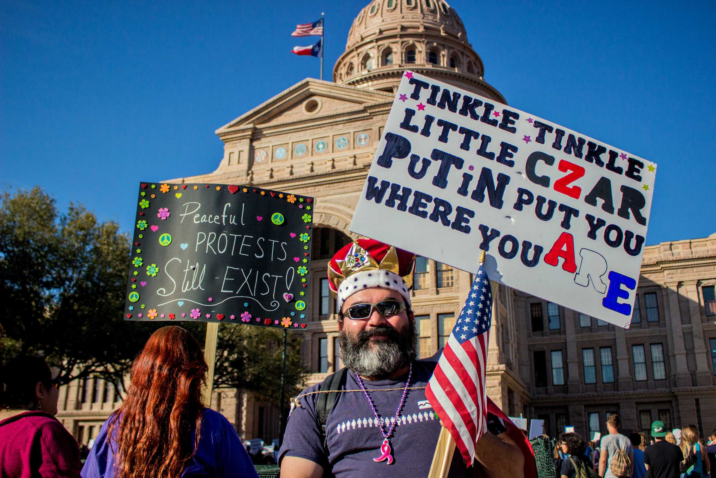   A man wearing a crown holds a sign that says, "Tinkle, tinkle little czar Putin put you where you are" in front of the Capitol.  